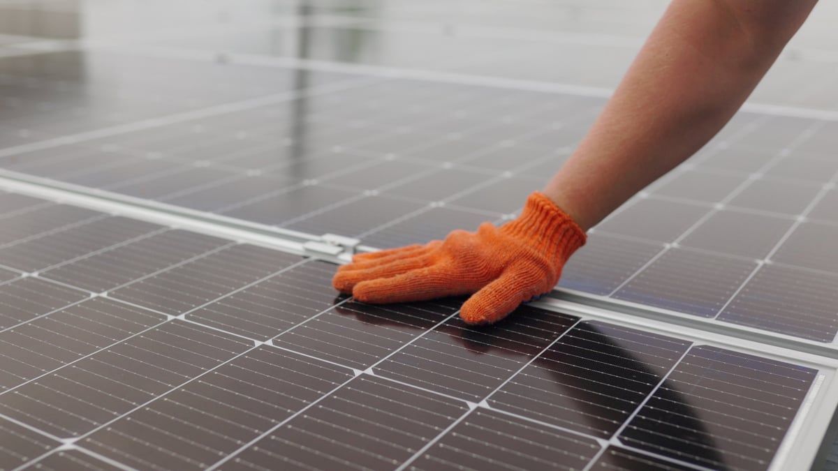 Unrecognizable man glove wiping solar panel from dust on sunny day. Close up of a young engineer hand is checking the operation of sun and cleanliness of photovoltaic solar panels on a sunset