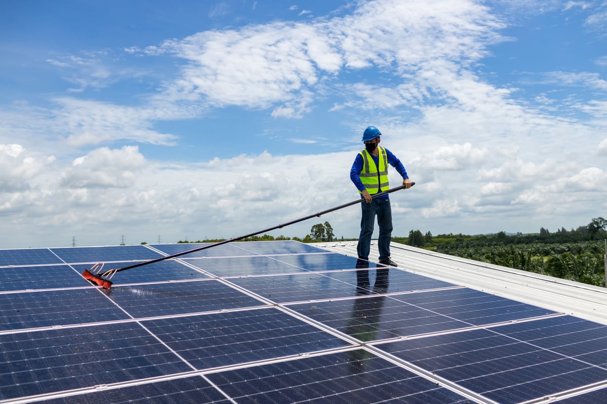 Worker cleaning solar panels with brush and water at a solar energy power plant
