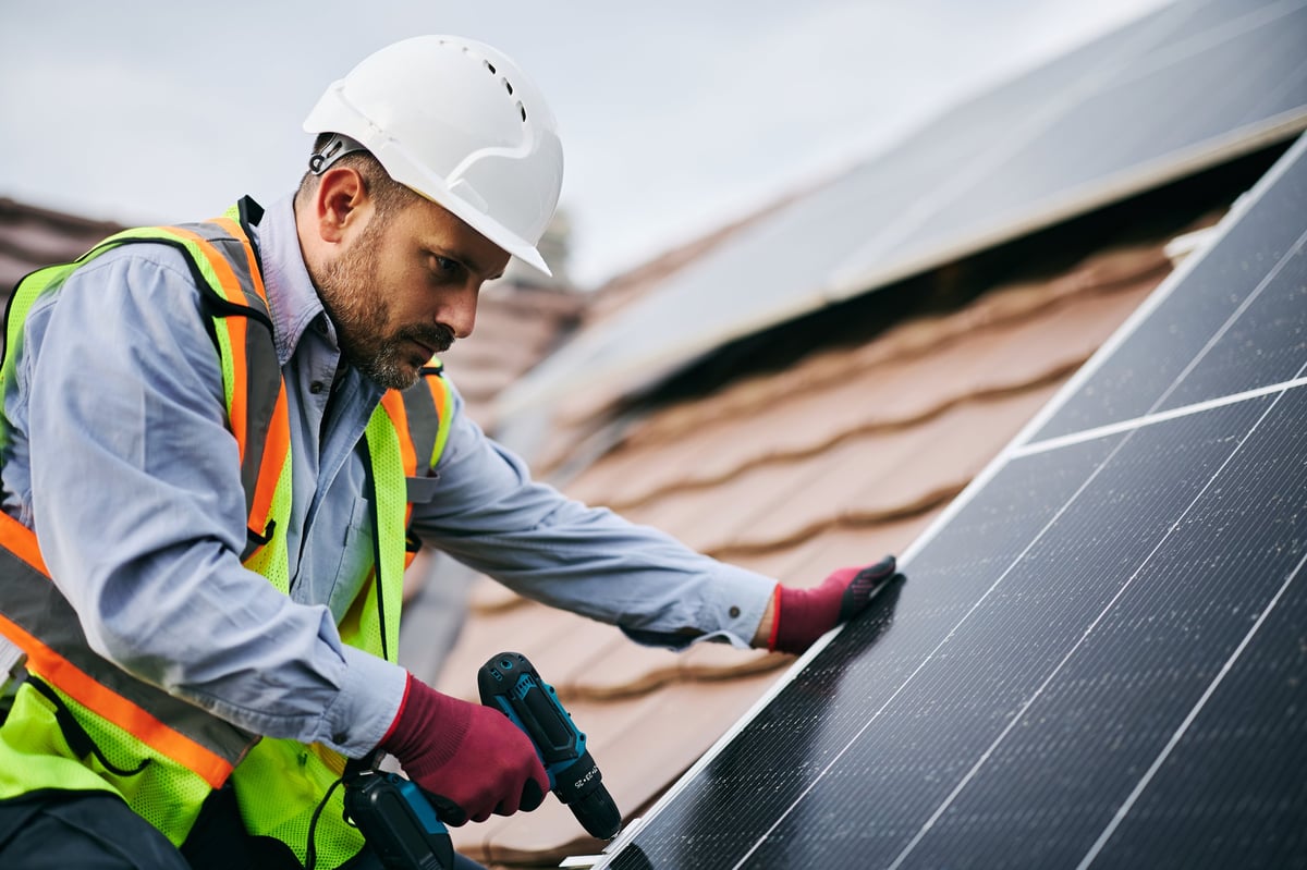 Mid adult engineer working on solar panel installation on the roof of the house.