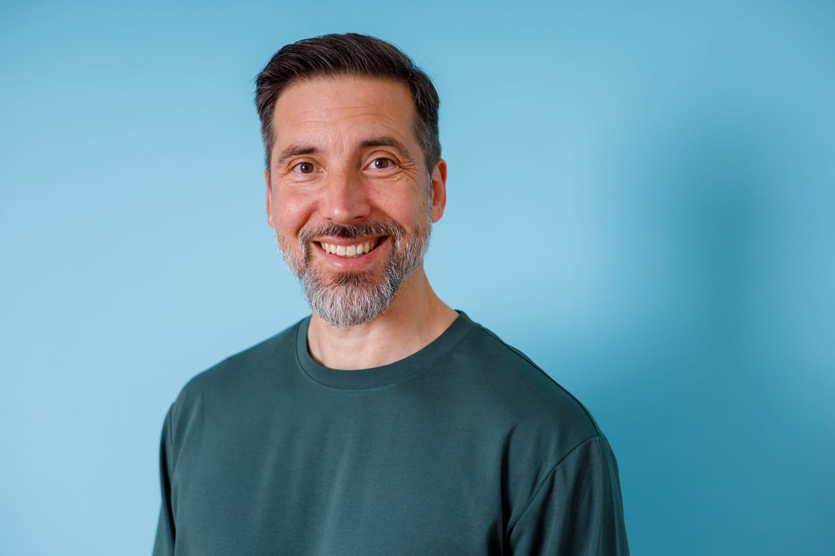 Friendly grey-bearded man smiling confidently in a casual t-shirt headshot