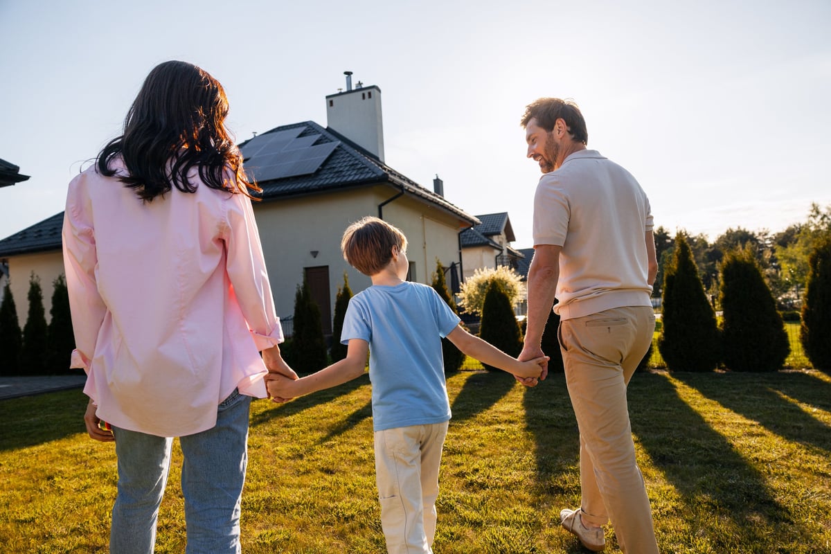 Family walking in backyard towards a residential house with solar panels at sunset