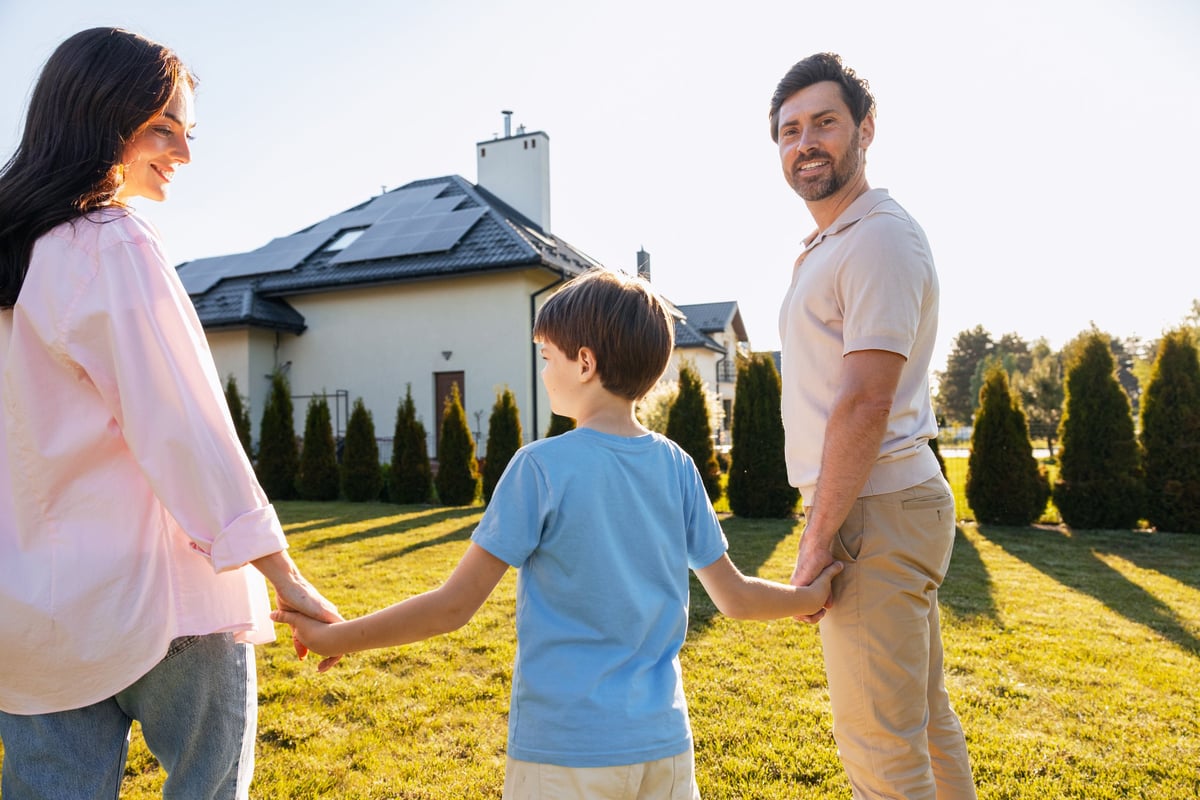Happy family standing in backyard of their home with solar panels, embracing sustainable living and home ownership