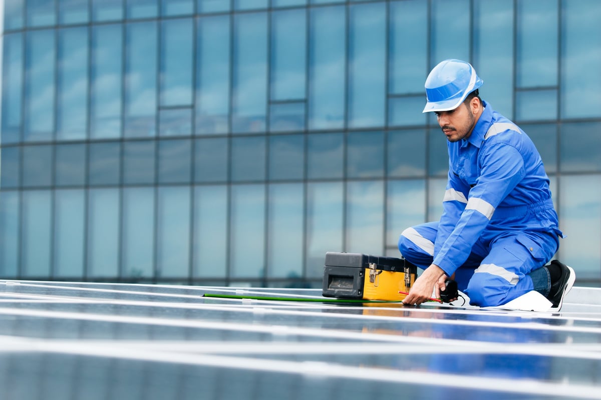 Solar technician kneels on rooftop panel array with open toolbox
